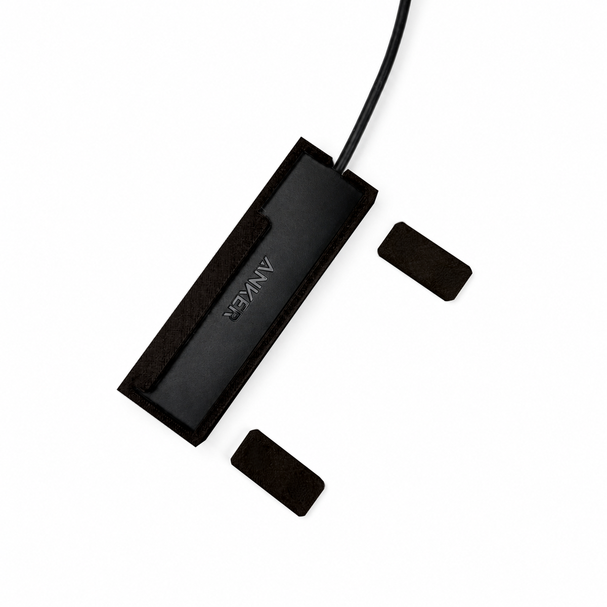Top view of black HubMount magnetic case holding an Anker USB hub, with adhesive magnetic feet positioned beside it.