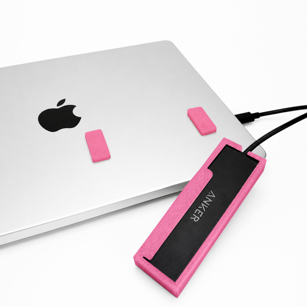 Front view of a light pink HubMount holding an Anker USB hub on a MacBook lid, with adhesive magnetic feet attached above the case.