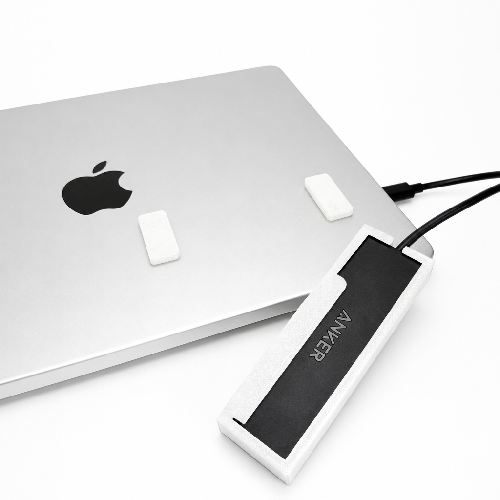 Front view of a white HubMount holding an Anker USB hub on a MacBook lid, with adhesive magnetic feet attached above the case.